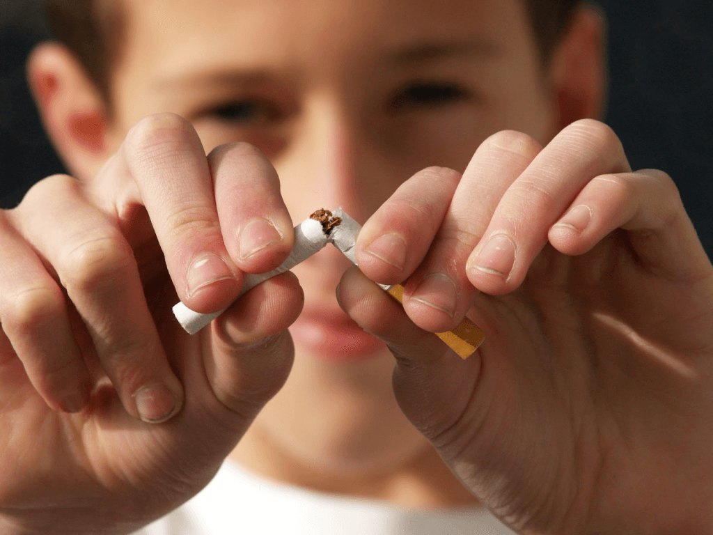 A boy is holding two cigarettes in his hands.